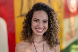 A smiling person with curly hair stands in front of a colorful blurred background, reminiscent of Charlie Patric's vibrant photography style.