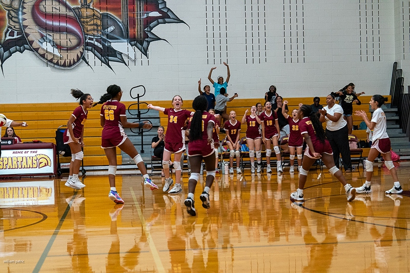The Stafford Volleyball - 7th Grade girls' team, dressed in maroon uniforms, celebrates enthusiastically on the court and sidelines, while their bench players and some spectators cheer loudly in the background.