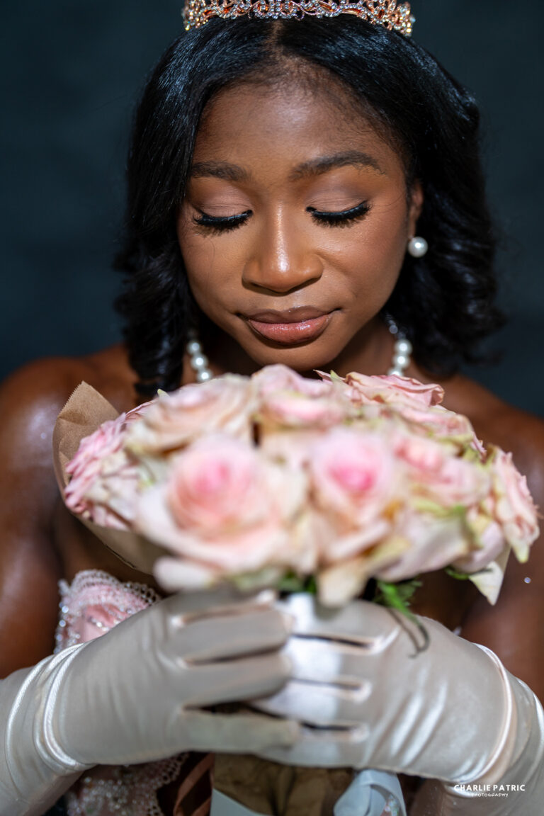 A woman wearing a tiara and white gloves holds a bouquet of pale pink roses close to her face with her eyes closed, capturing the elegance highlighted in Frisco senior photography packages.