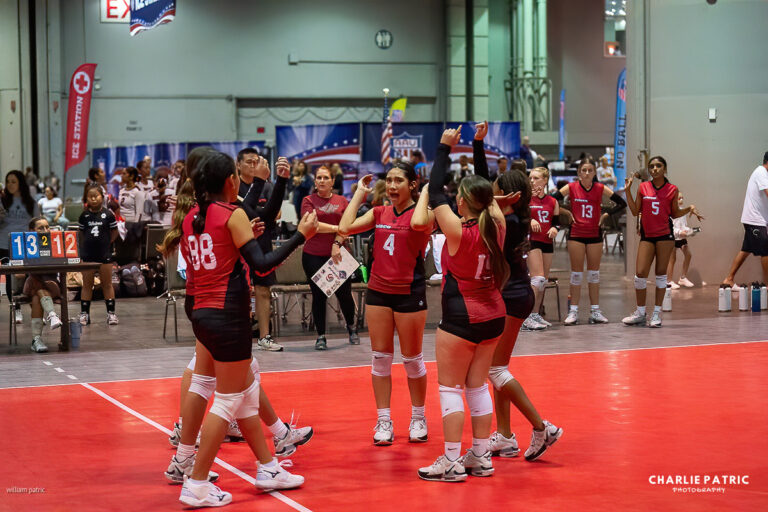 A girls' volleyball team in red uniforms celebrates on an indoor court, with other teams and spectators in the background—perfect for editing sports photos to capture the excitement of the game.