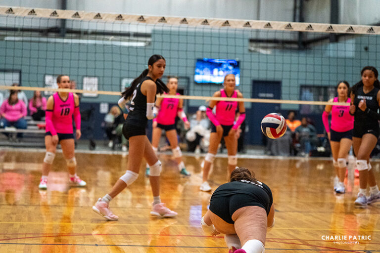 A volleyball player dives for the ball as teammates and opponents watch on an indoor court during a match, captured in dynamic sports photography for college recruitment.