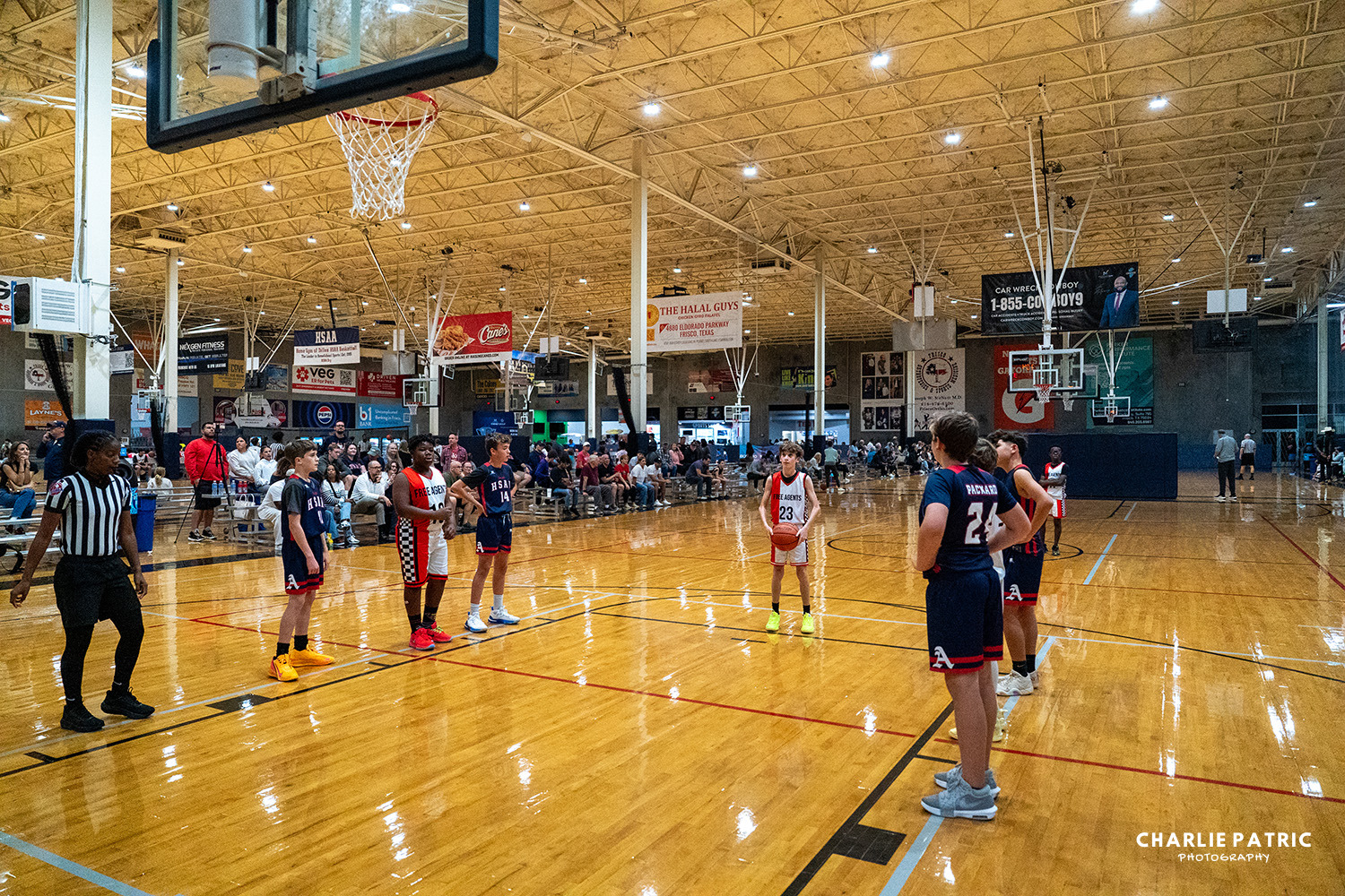 A youth basketball game is underway in an indoor gym, with players lined up for a free throw as spectators watch from the bleachers—a perfect moment for sports photography enthusiasts.
