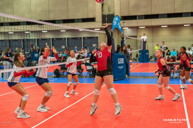 A youth volleyball player in a red jersey prepares to set the ball while teammates and opponents watch on an indoor court—a perfect moment captured by expert youth sports photography services.