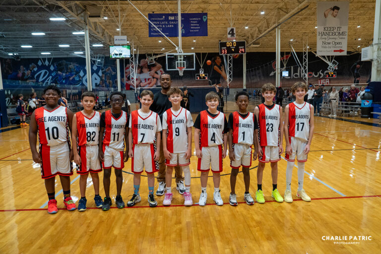 Eleven young boys in matching "Free Agents" basketball uniforms stand in a row on an indoor basketball court, smiling for a group photo captured by youth sports photography services.