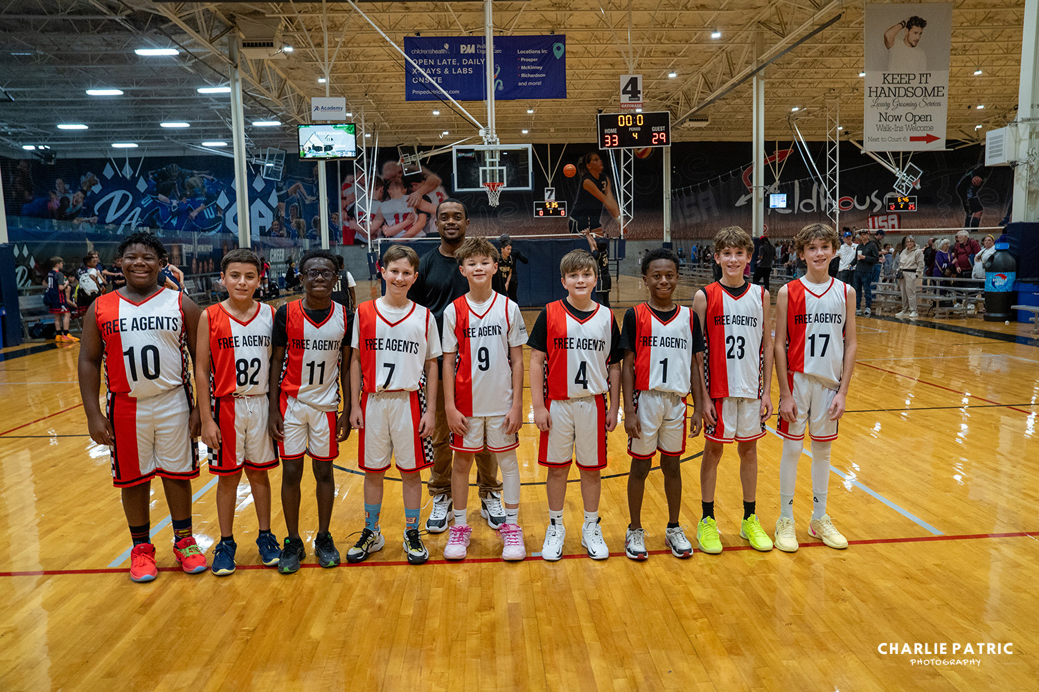 Eleven young boys in matching "Free Agents" basketball uniforms stand in a row on an indoor basketball court, smiling for a group photo captured by youth sports photography services.