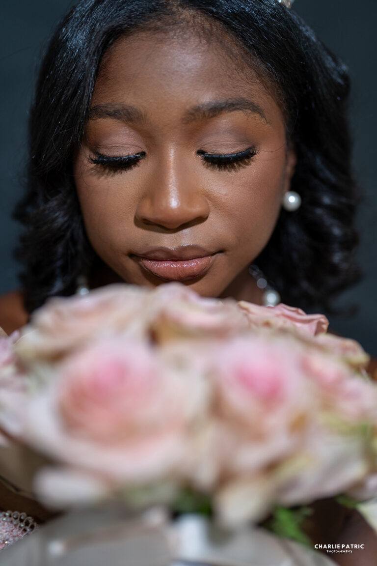 A woman with closed eyes holds a bouquet of pink and white roses close to her face, wearing pearl earrings and a necklace, captured in the elegant style of Frisco graduation photography services.
