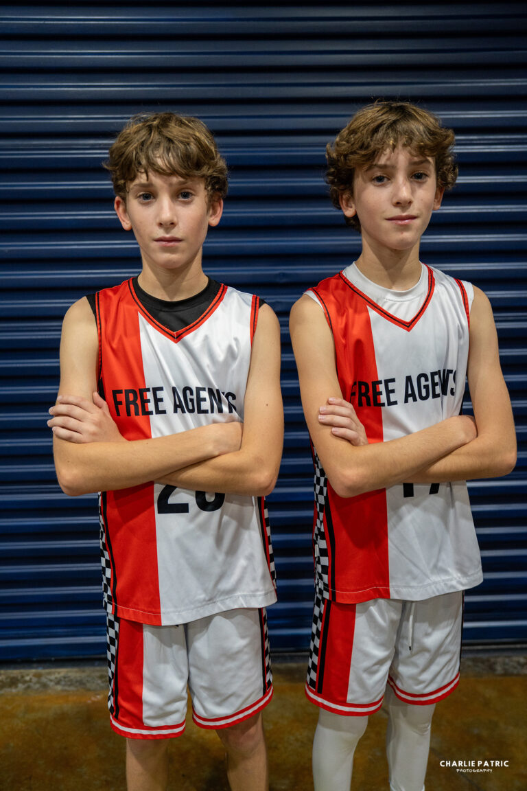 Two boys in matching “Free Agents” basketball uniforms stand side by side with arms crossed in front of a blue garage door, their confident poses perfectly captured by a Frisco sports event photographer.
