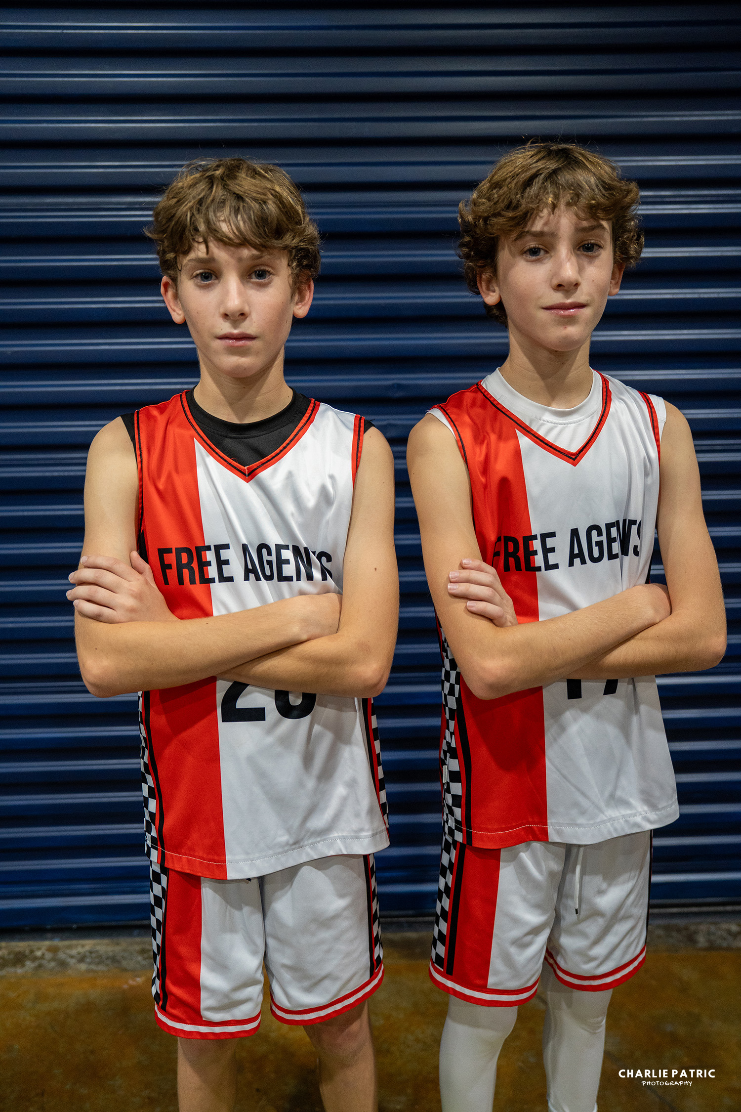 Two boys in matching “Free Agents” basketball uniforms stand side by side with arms crossed in front of a blue garage door, their confident poses perfectly captured by a Frisco sports event photographer.