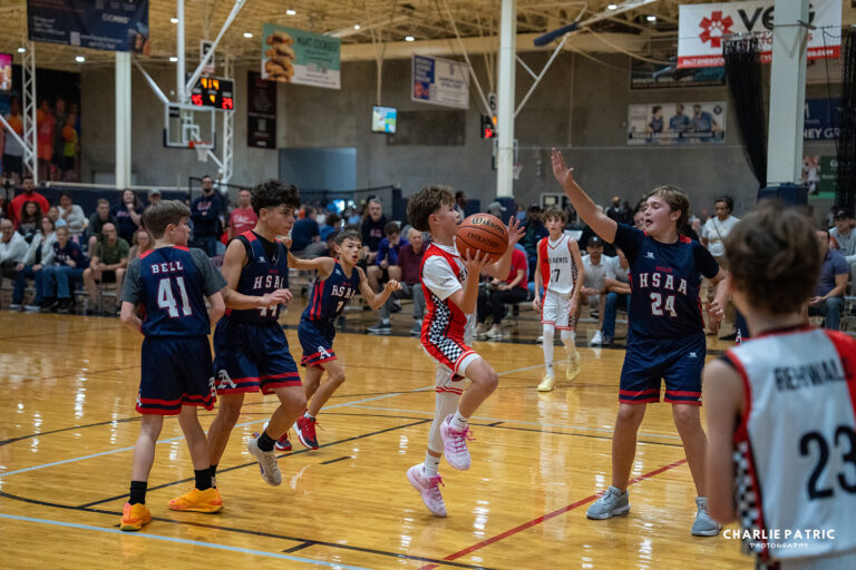 A youth basketball player prepares to shoot while being defended by opposing players during a game in a gymnasium with spectators in the background, expertly captured by a Frisco sports event photographer.