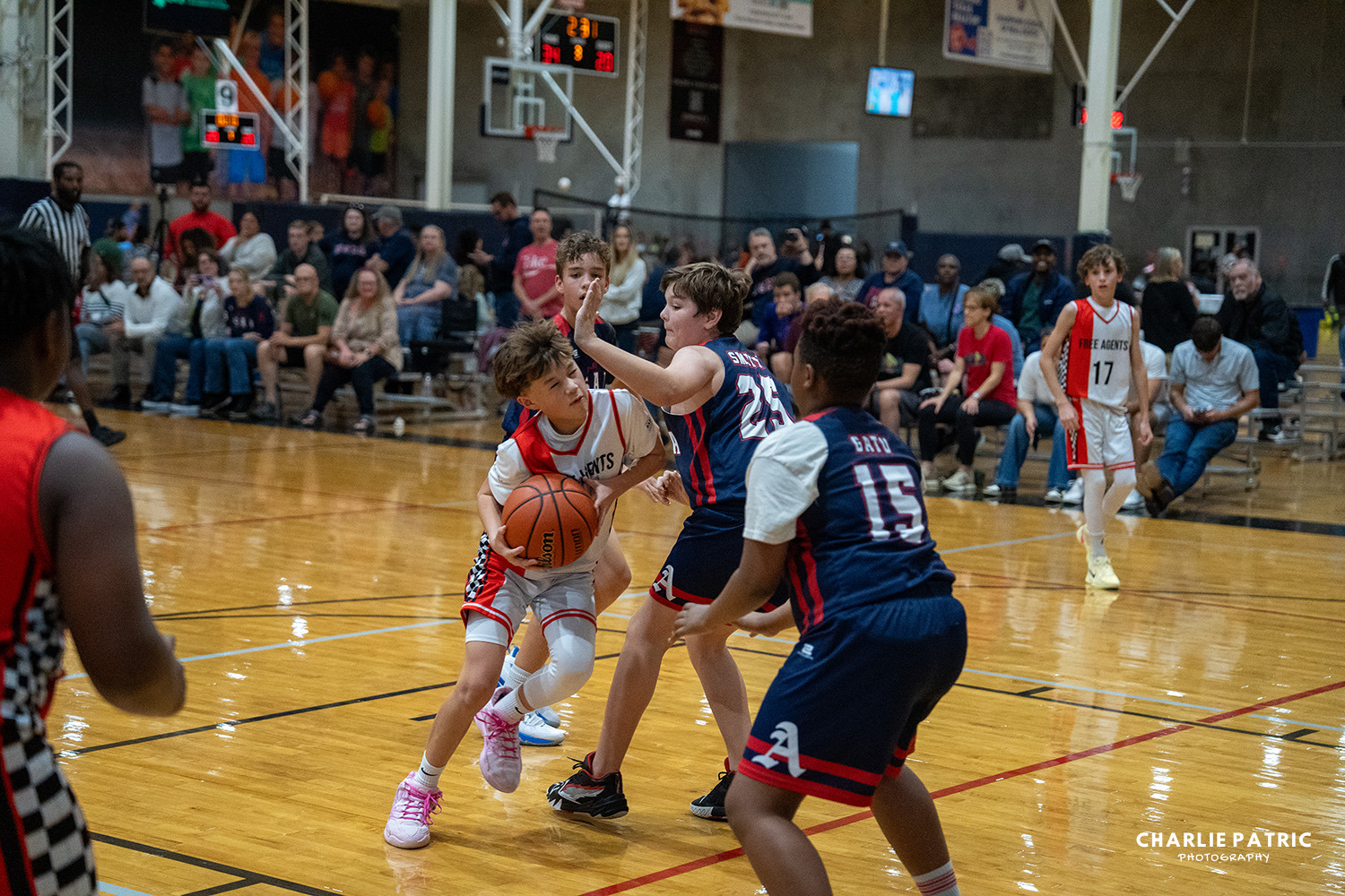 A Frisco sports event photographer captures a basketball player in a white uniform driving to the hoop while being guarded by two players in blue uniforms.